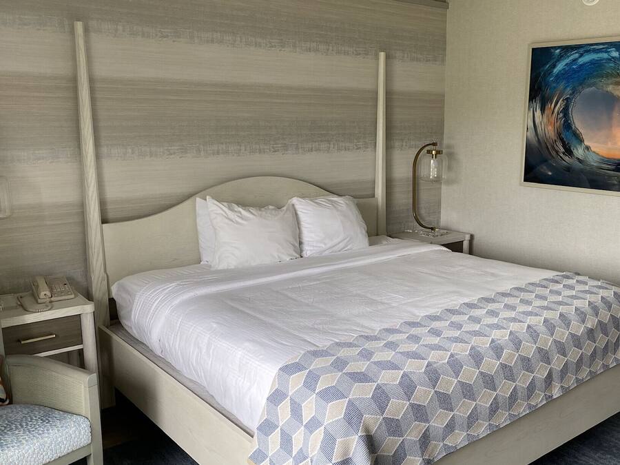 A hotel room with a bed, a nightstand, a telephone, and a painting on the wall.