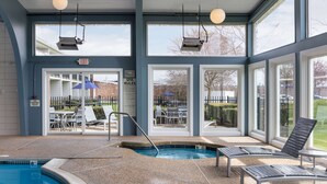 An indoor pool area with clear glass walls, a pool, and lounge chairs. - Howard Johnson by Wyndham Middletown Newport Area (Middletown)