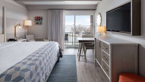 A hotel room with a bed, desk, TV, and a balcony with a view. - Howard Johnson by Wyndham Middletown Newport Area (Middletown)