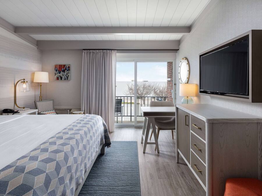 A hotel room with a bed, desk, TV, and a balcony with a view.