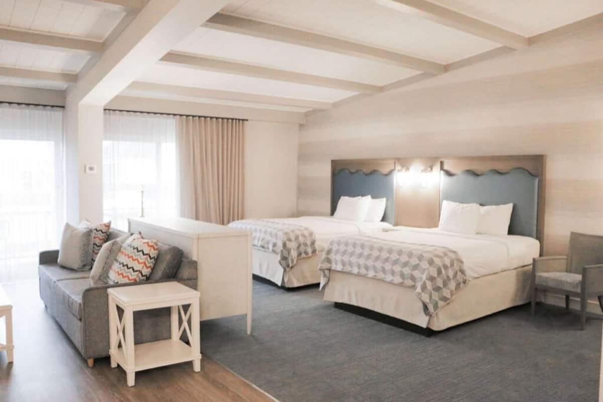 A hotel room with two beds, a sofa, a small table, and a chair.