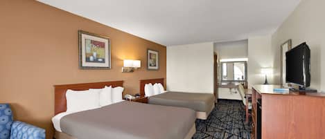 Habitación de hotel con dos camas, un escritorio con televisor, una silla y un baño visible a través de una puerta abierta.