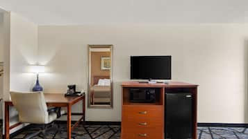 Une chambre d’hôtel équipée d’un bureau, d’une chaise, d’une télévision, d’un four à micro-ondes et d’un miroir.