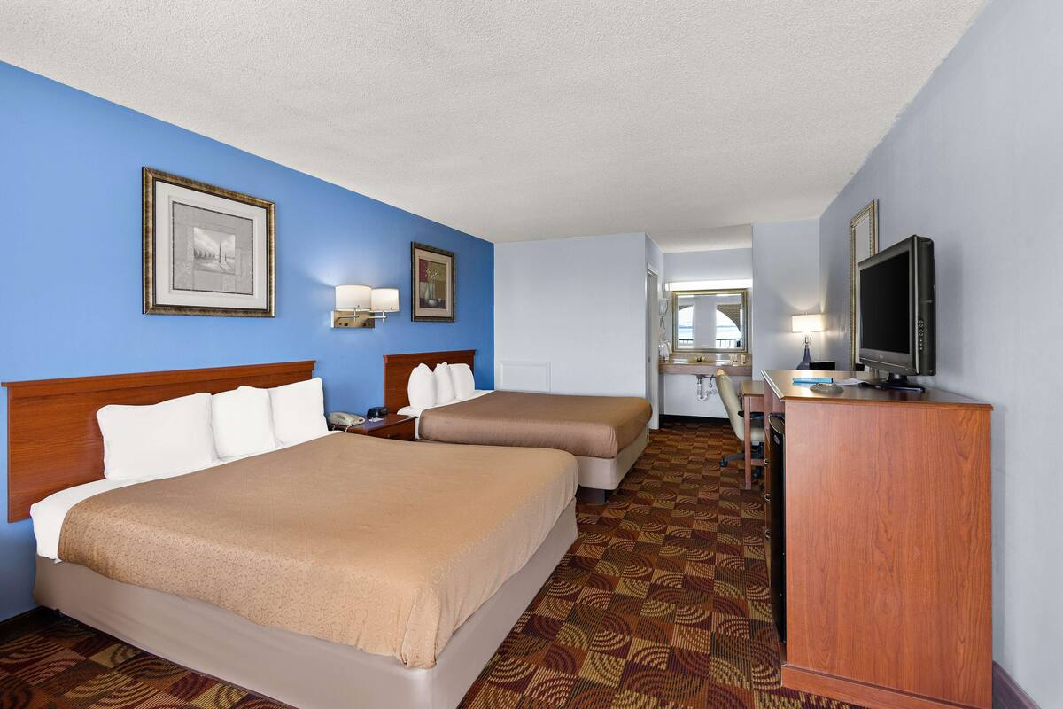 A hotel room with two beds, a television, a desk, and a mirror.