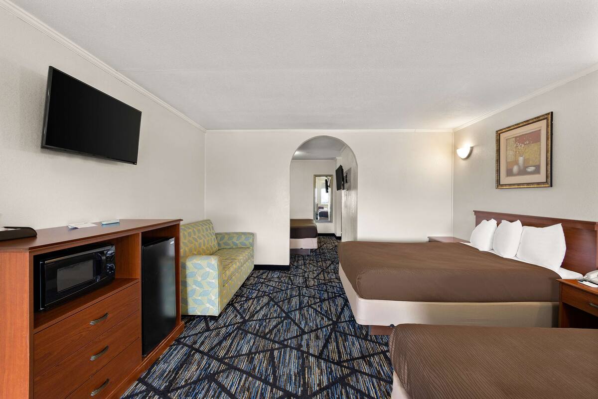 A hotel room with a bed, a desk with a microwave, a small seating area, and a television on the wall.