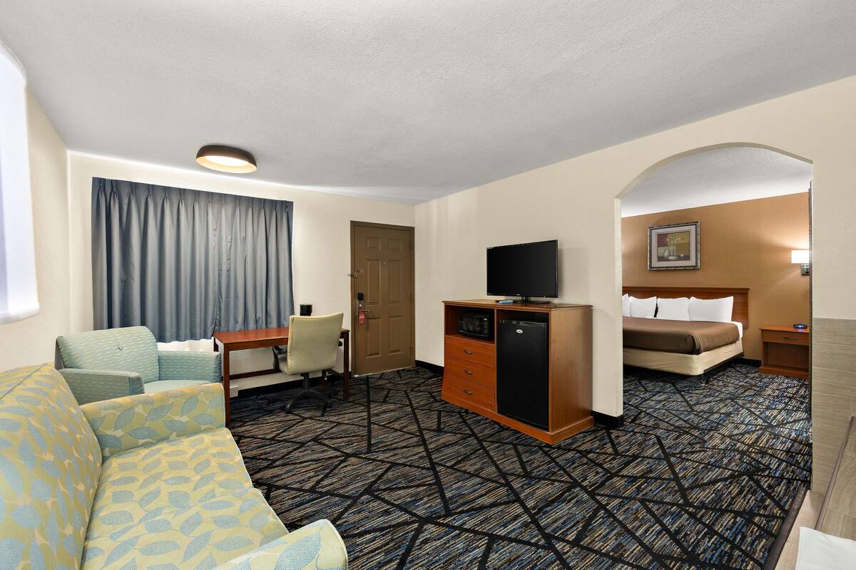 A hotel room with a sofa, a desk, a television, a bed, and a patterned carpet.