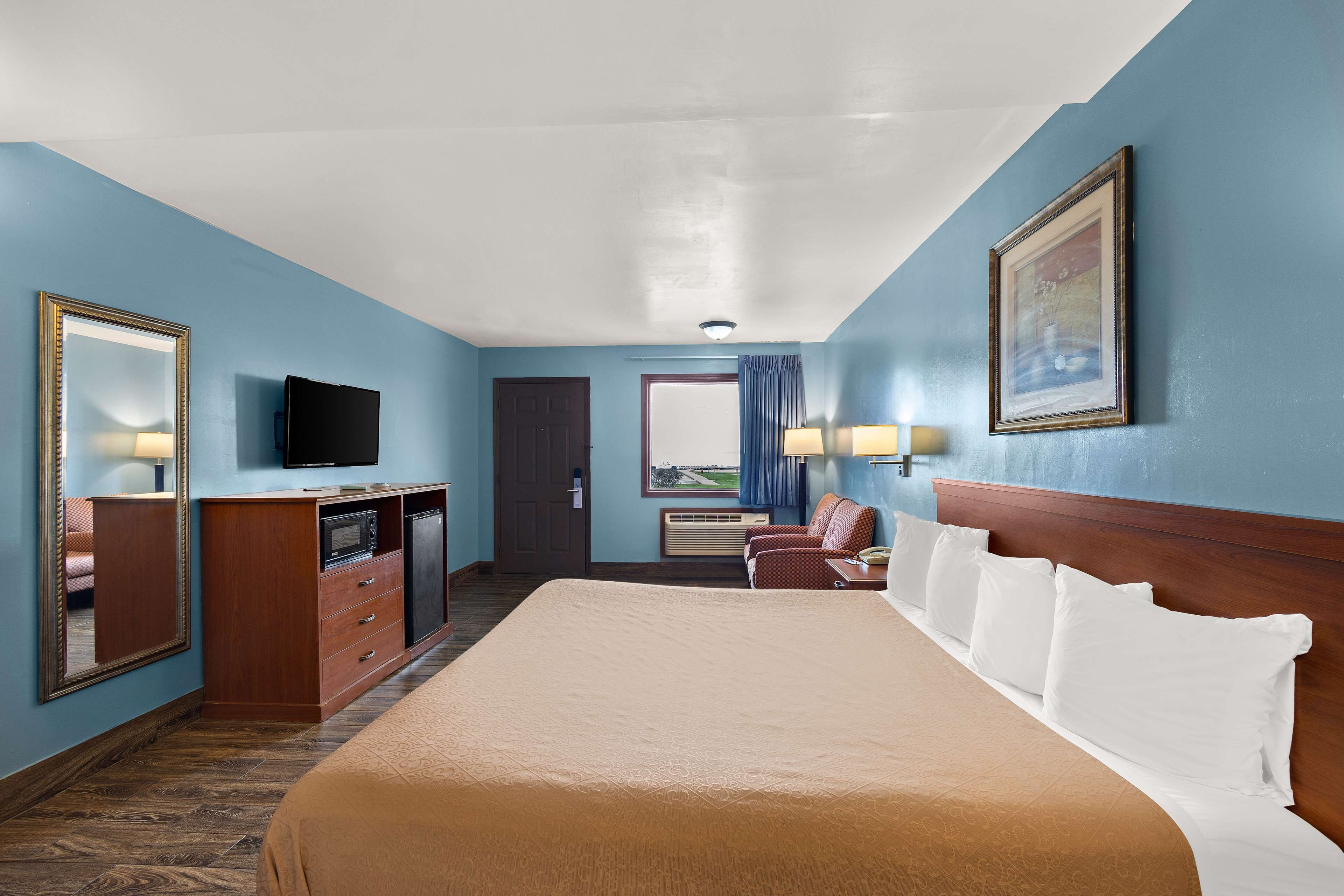 Habitación de hotel con una cama grande, un escritorio con televisor, cómoda y una puerta que da a un balcón.