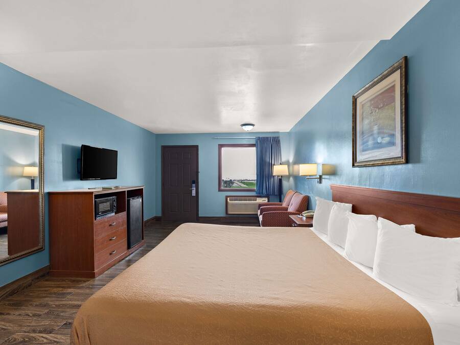 A hotel room with a large bed, a desk with a television, a dresser, and a door leading to a balcony.