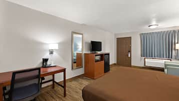 Habitación de hotel con cama, escritorio con silla, televisor, espejo, armario y ventana con cortinas.