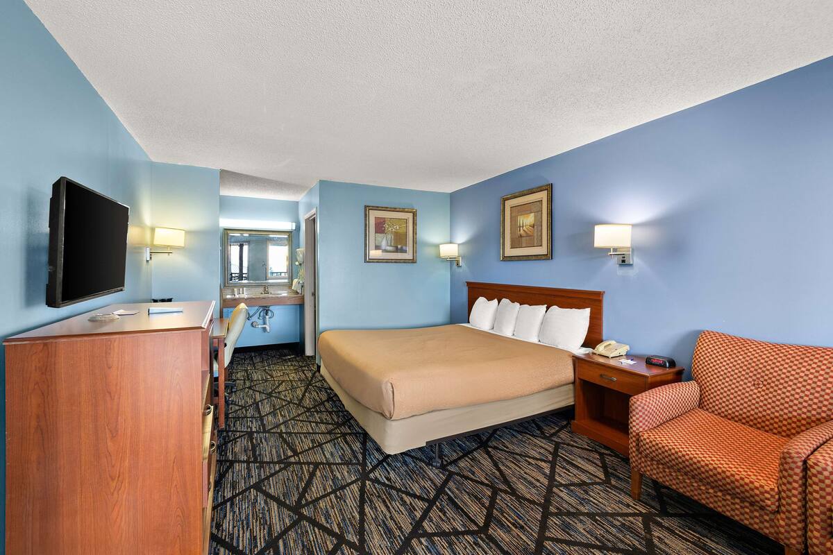 A hotel room with a bed, a desk, a television, a chair, and a mirror.