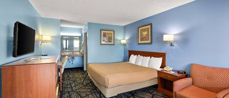 A hotel room with a bed, a desk, a television, a chair, and a mirror.