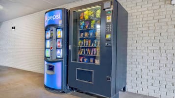 A vending machine with a Pepsi logo and a snack vending machine next to a white brick wall.