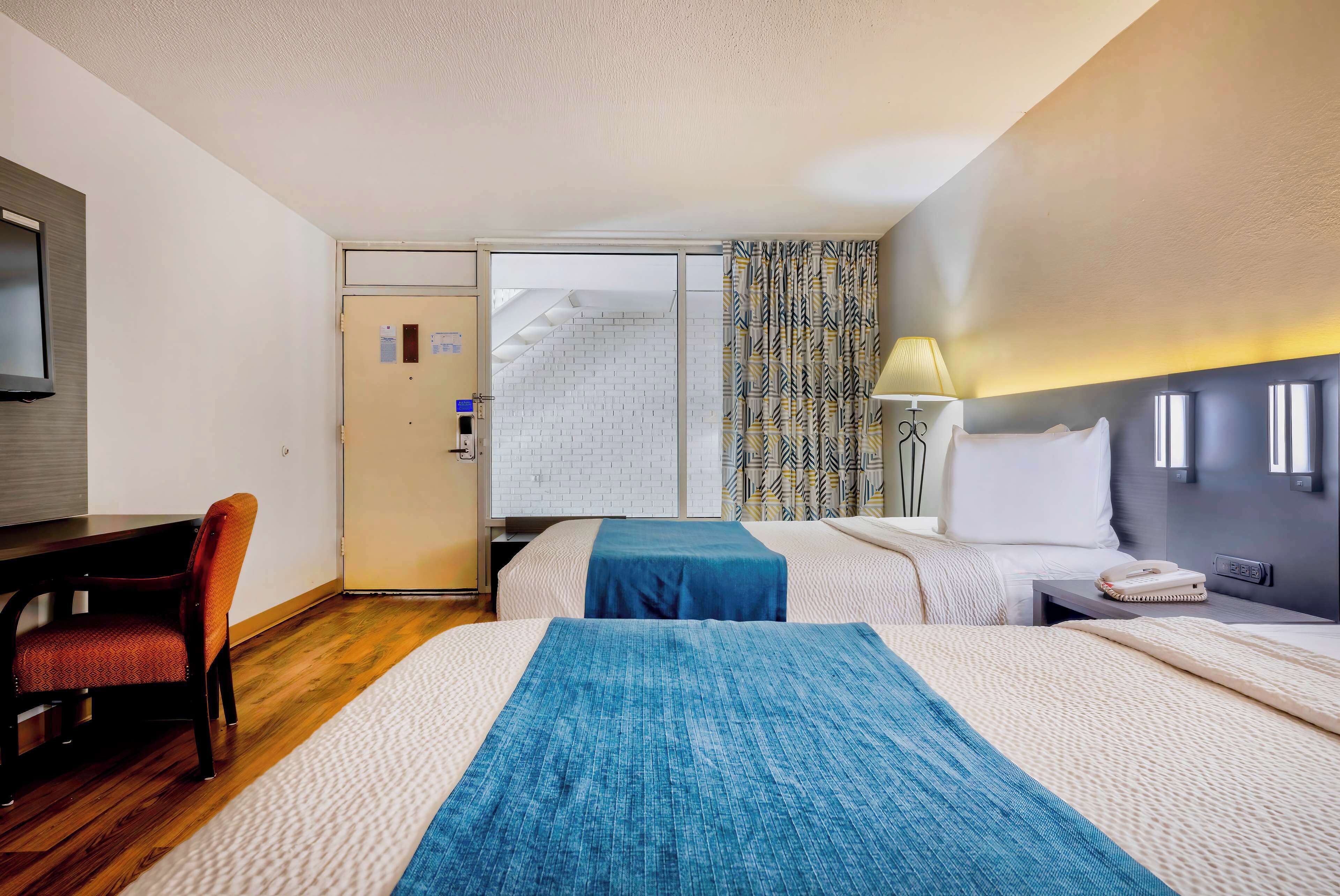 Habitación de hotel con dos camas, un escritorio, una silla, un televisor y una ventana con cortinas.