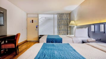 Habitación de hotel con dos camas, un escritorio, una silla, un televisor y una ventana con cortinas.