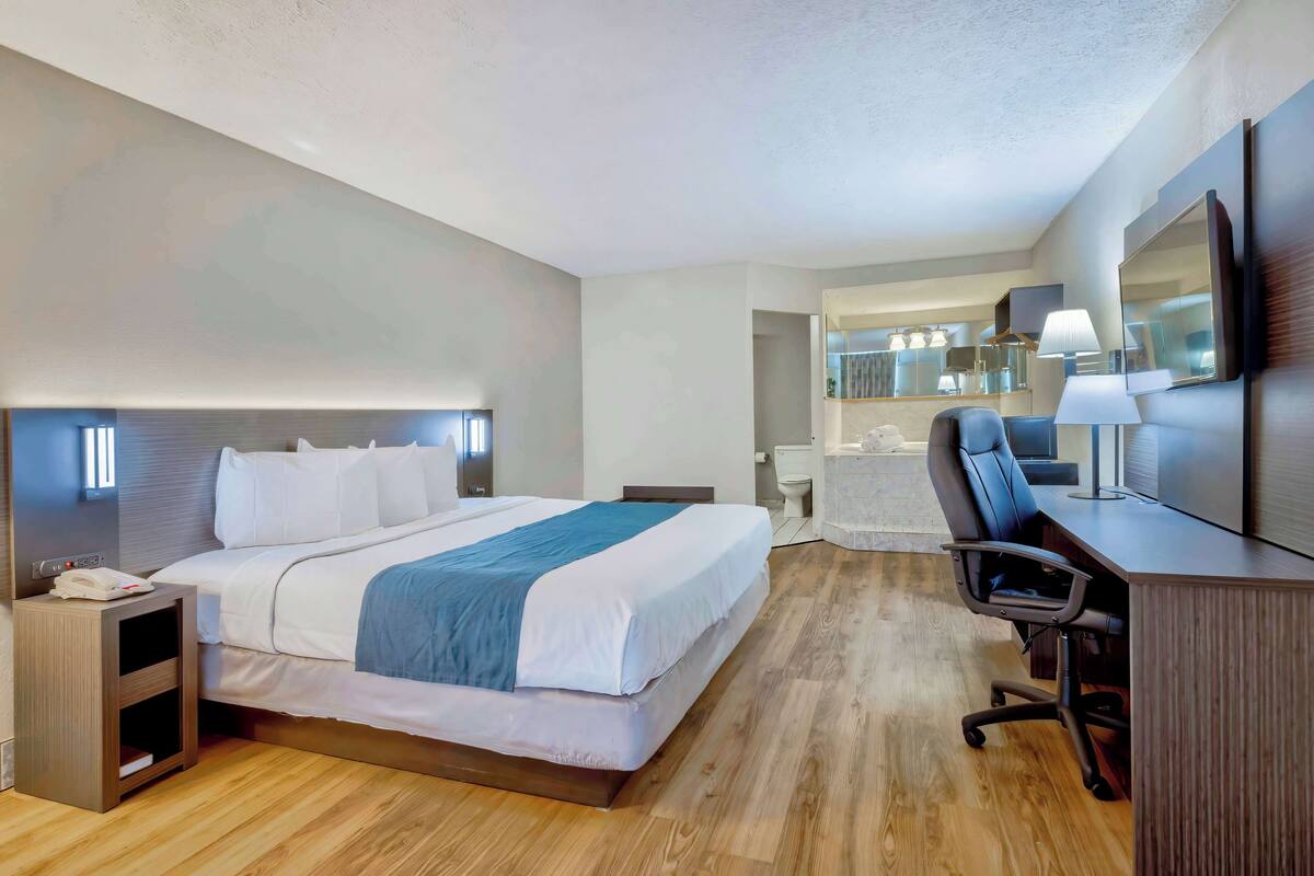 A hotel room with a bed, desk, chair, and a large mirror.