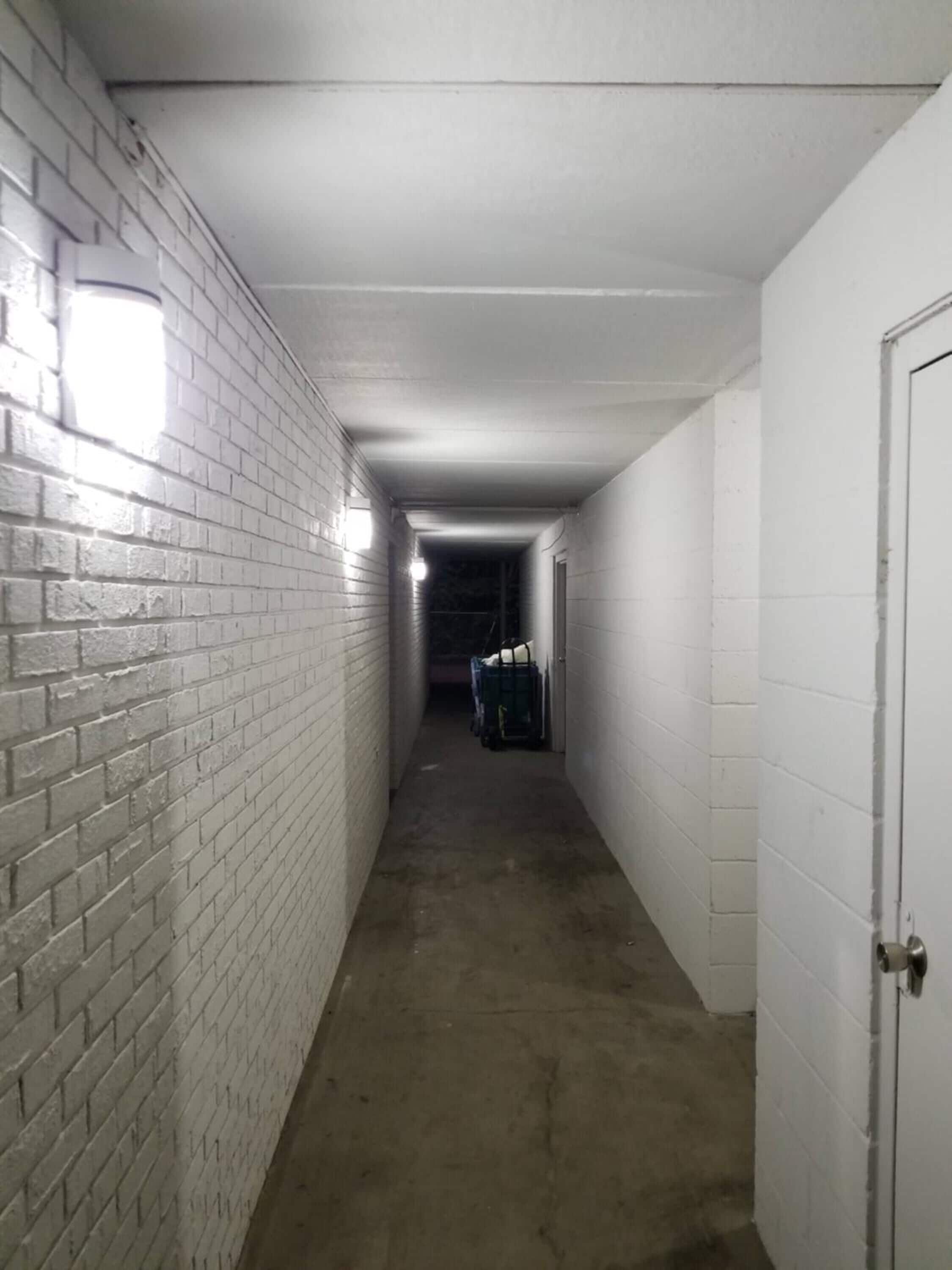 A narrow, dimly lit corridor with white brick walls and a concrete floor.