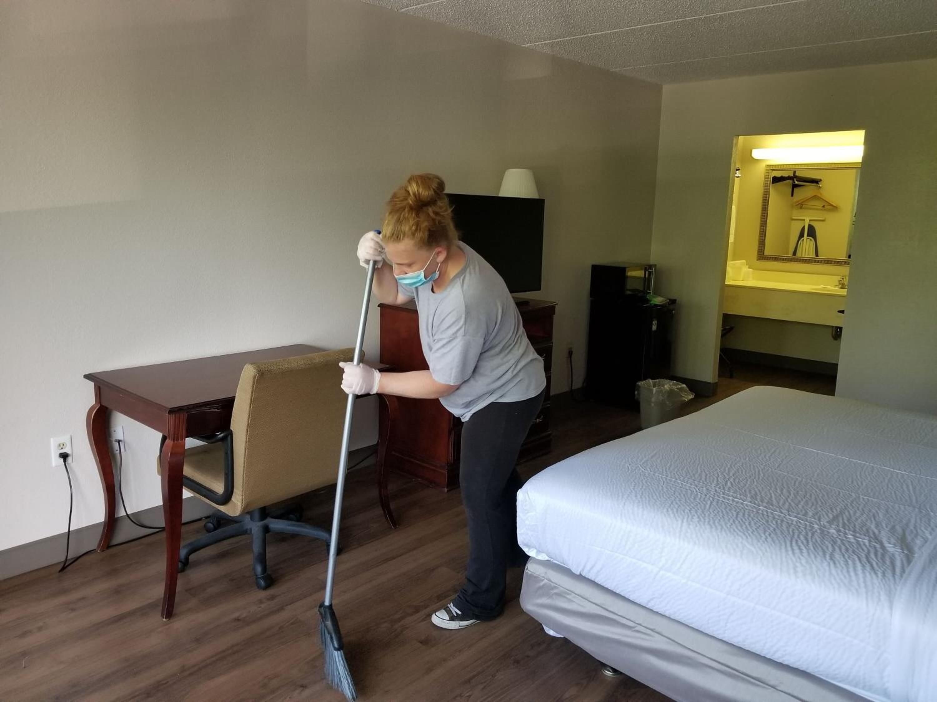 A hotel room with a bed, a desk, a chair, and a broom.
