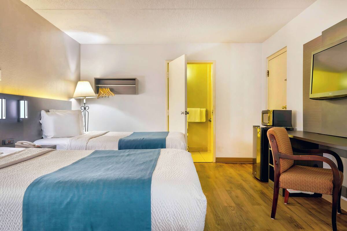 A hotel room with two beds, a desk, a chair, a TV, and a wardrobe.