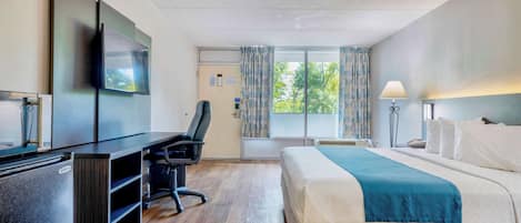 A hotel room with a bed, desk, chair, TV, and a window with curtains.