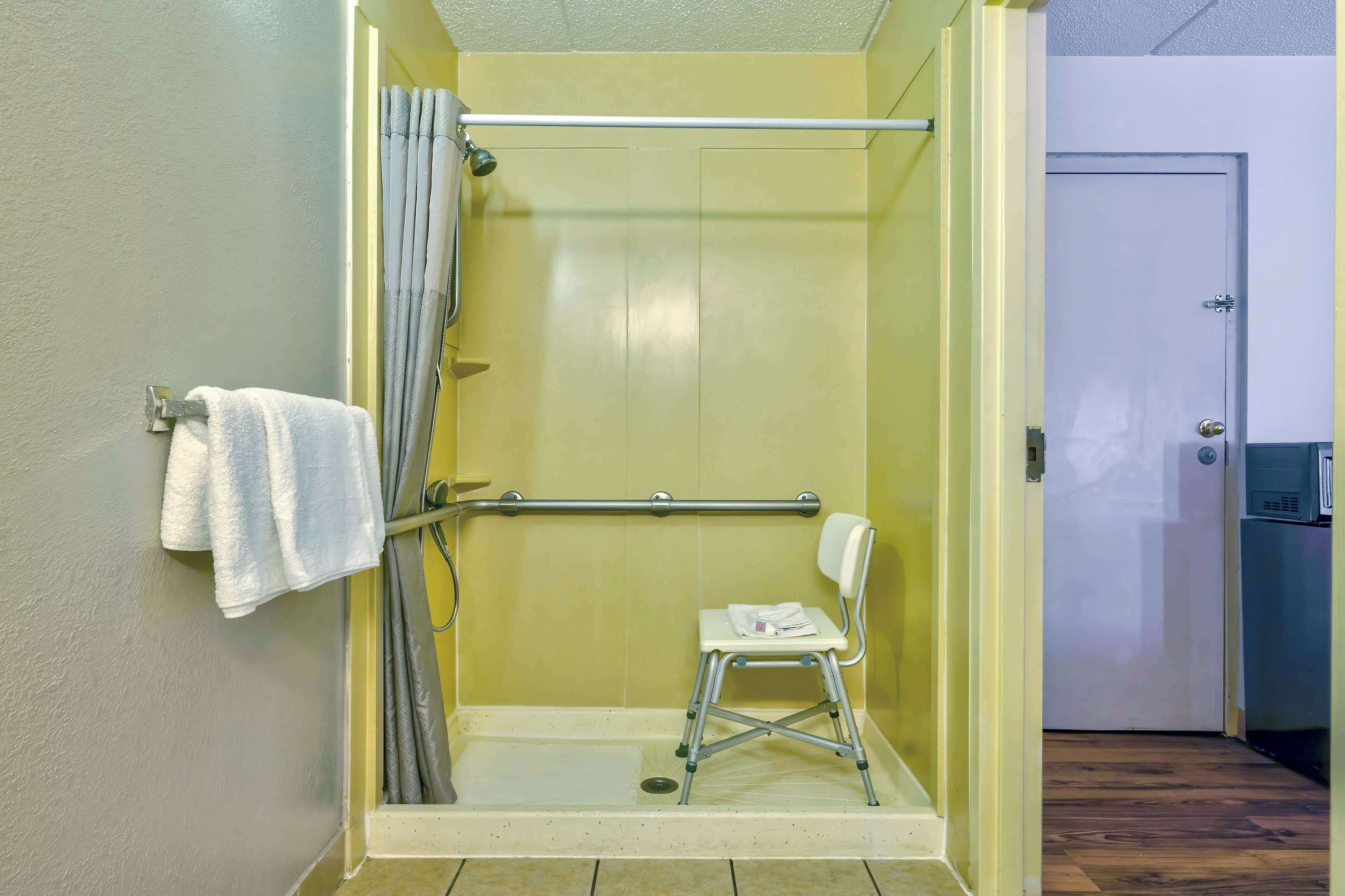 A shower with a white chair, a towel rack, and a door leading to a room.