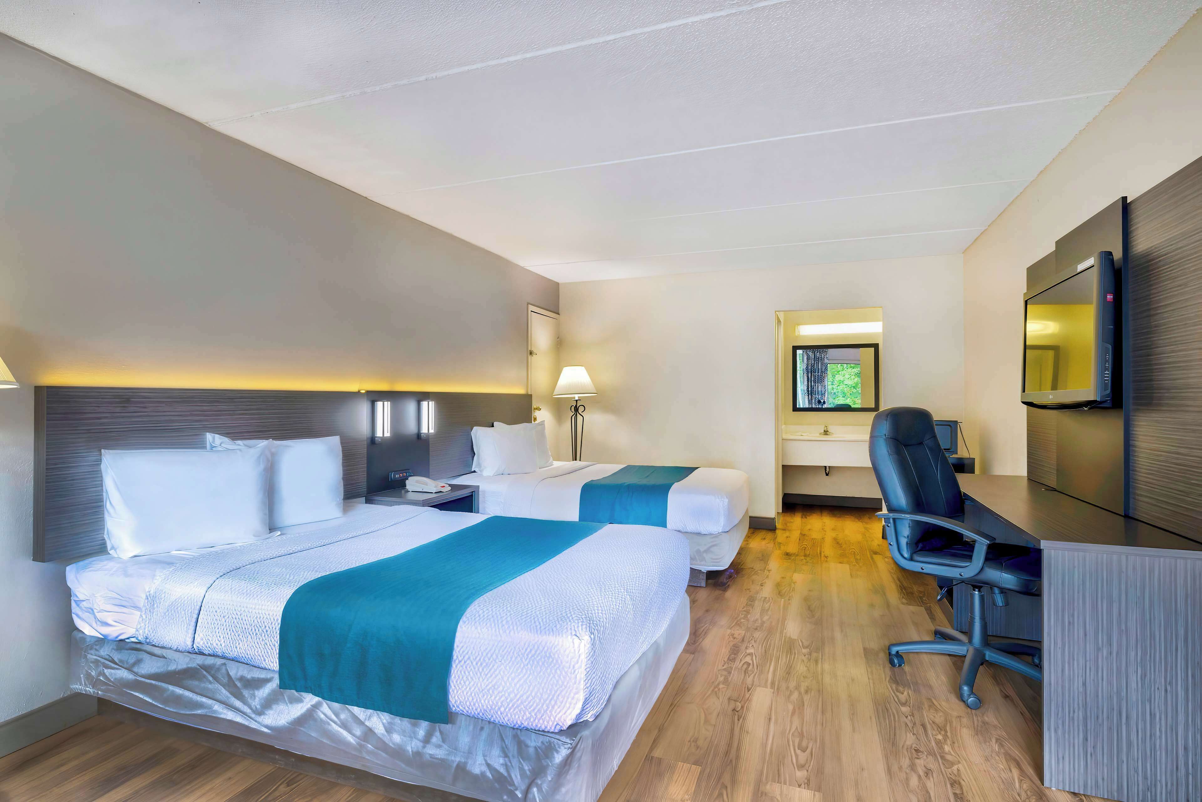 A hotel room with two beds, a desk, a chair, a TV, and a mirror.