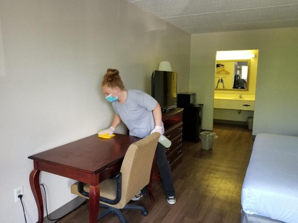 A hotel room with a wooden desk, a chair, a bed, a mirror, and a television.