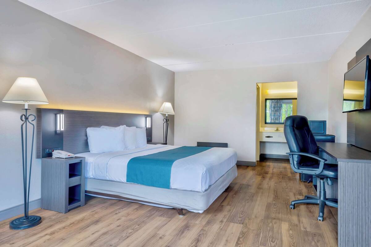 A hotel room with a bed, bedside lamps, a desk with a chair, and a flat-screen TV.