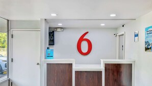 A reception area with a large red number '6' on the wall, wooden reception desks, and a door to the left. - Motel 6 Morgantown, WV (Morgantown)