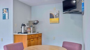 A small room with a round wooden table, two purple chairs, a coffee machine, a TV mounted on the wall, and a poster advertising coffee. - Motel 6 Morgantown, WV (Morgantown)