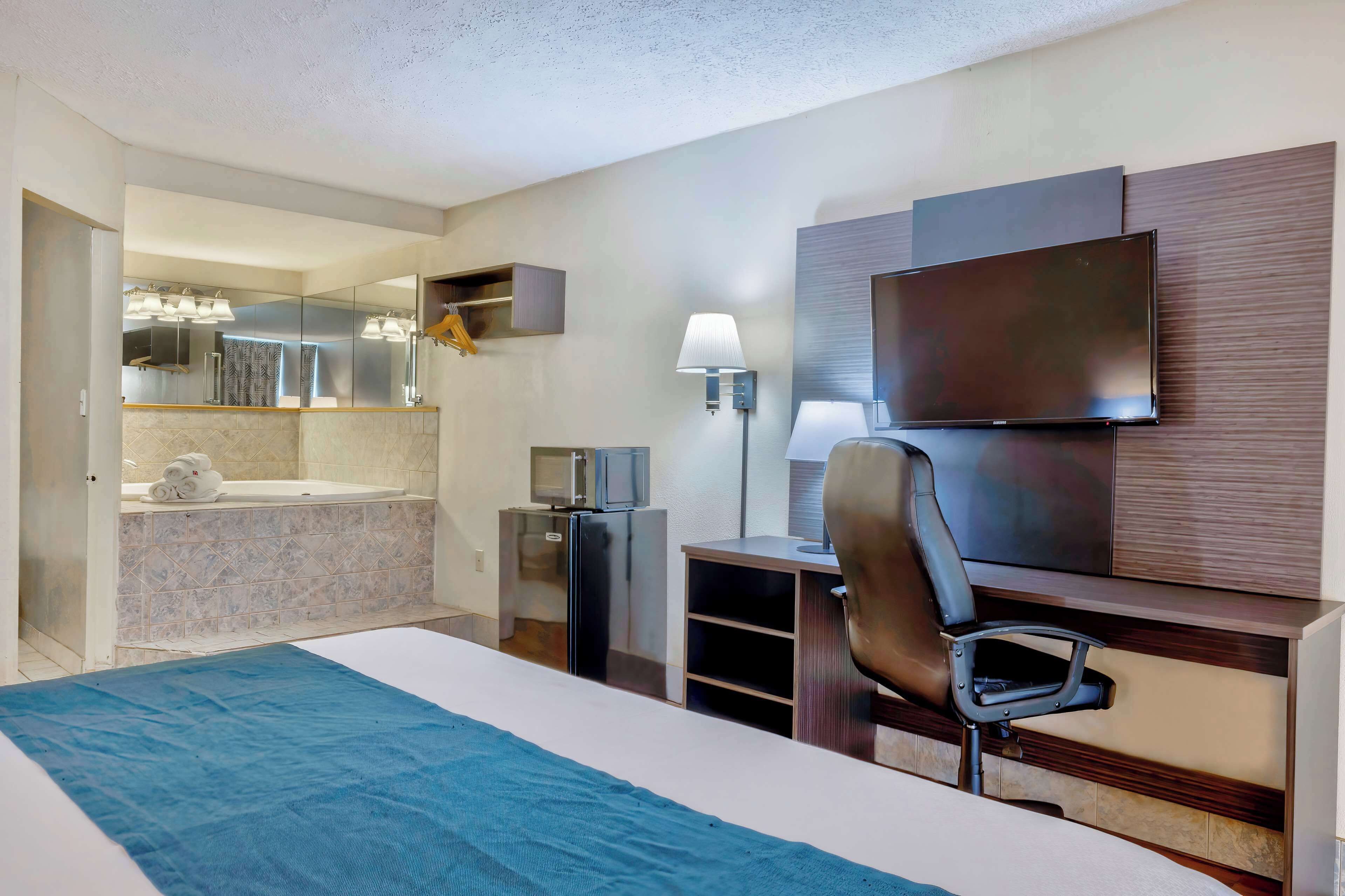 Ein Hotelzimmer mit Bett, Schreibtisch, Stuhl, Fernseher, Lampe, Mikrowelle und einer kleinen Küchenzeile.