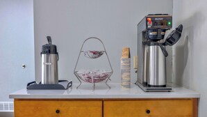 A kitchenette with a coffee maker, a water dispenser, and a stack of plates on a white countertop. - Motel 6 Morgantown, WV (Morgantown)