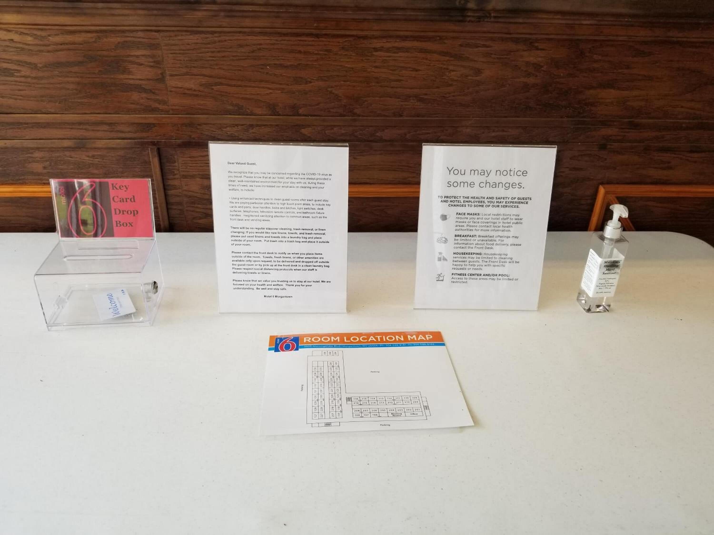 A hotel reception area with a welcome card, a key card drop box, a room location map, and a sanitizer bottle.