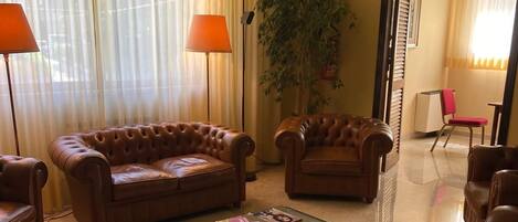 A hotel lobby with leather sofas, a glass coffee table, a potted plant, and a clock on the wall.