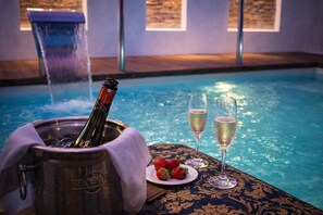 En miljö vid poolkanten med en champagneflaska i en hink, två champagneglas och jordgubbar på en tallrik.