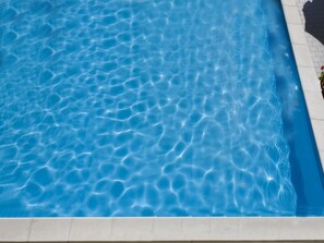 A clear blue pool with a tiled edge and a shadow of a person on the right side. - Hotel Savoy (Pesaro)