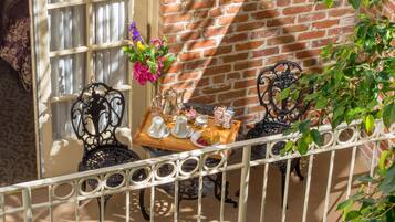 A balcony with a brick wall, a window with curtains, and two chairs with a tray of items.