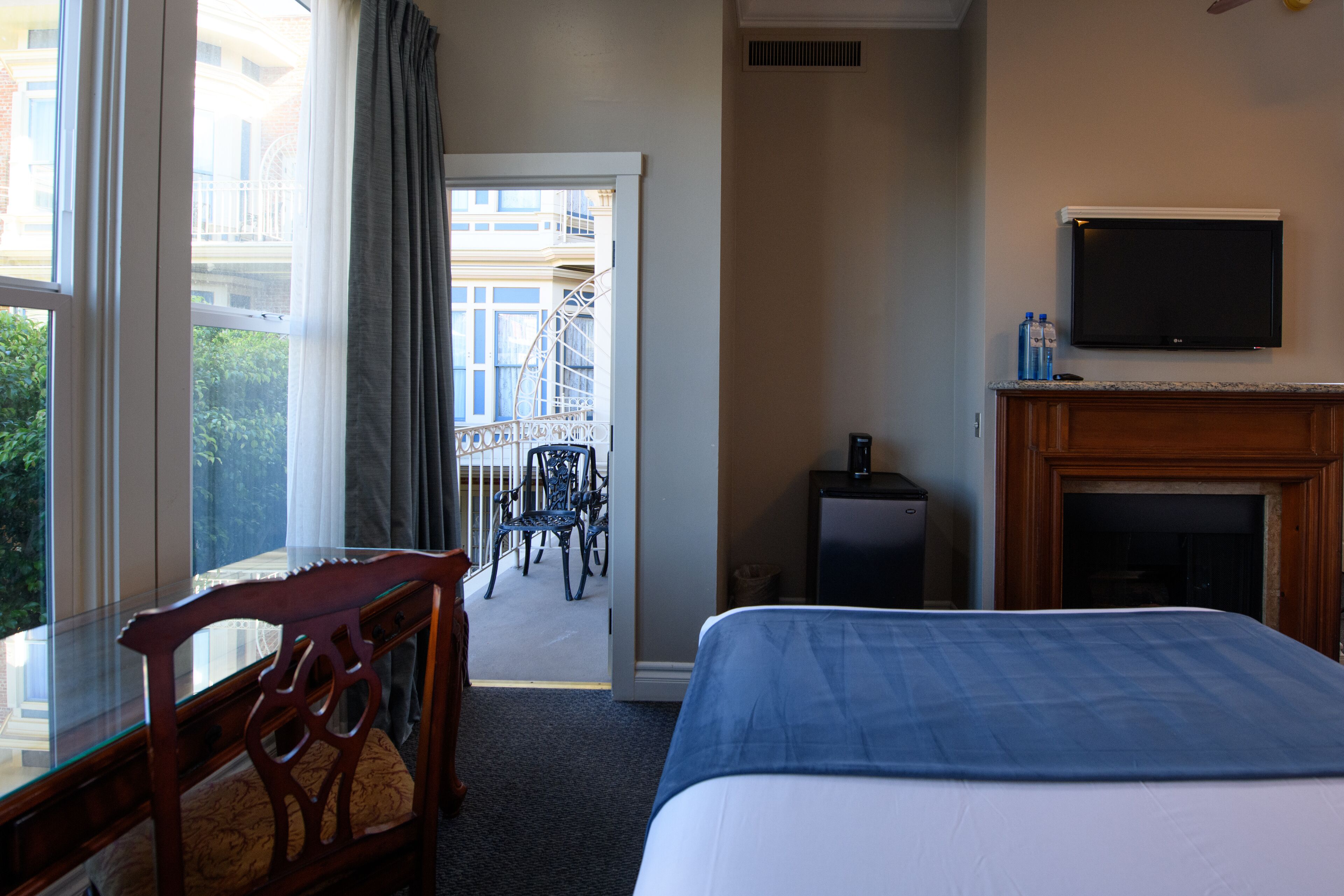 A hotel room with a bed, a TV, a fireplace, a desk, and a view of the outside balcony.