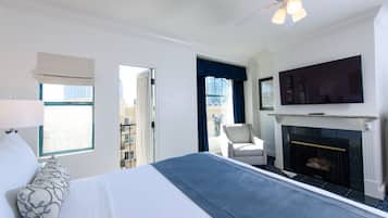 A hotel room with a bed, a television, a fireplace, and a view of the city.