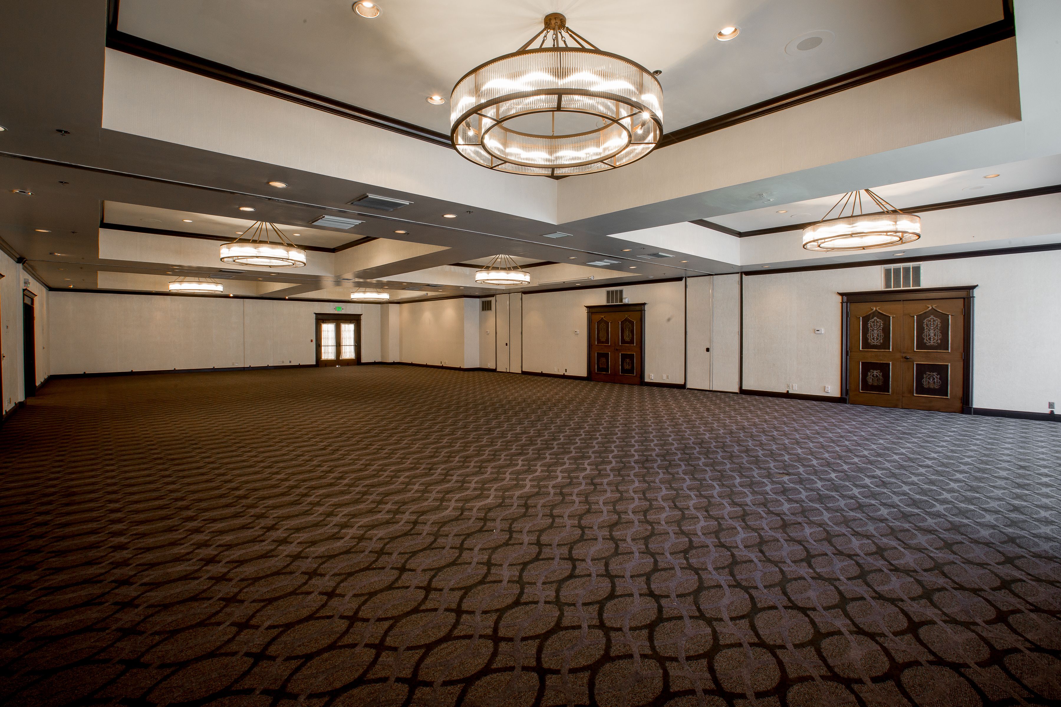 A large, empty conference room with patterned carpet, multiple chandeliers, and wooden doors.