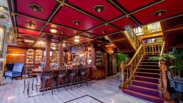 A bar area with a red ceiling, wooden bar counter, and multiple bar stools.
