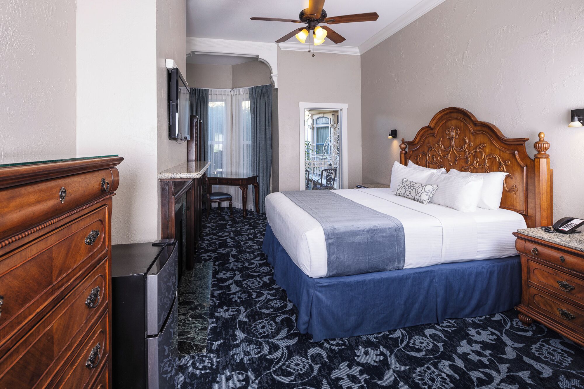 A hotel room with a bed, dresser, desk, and a ceiling fan.