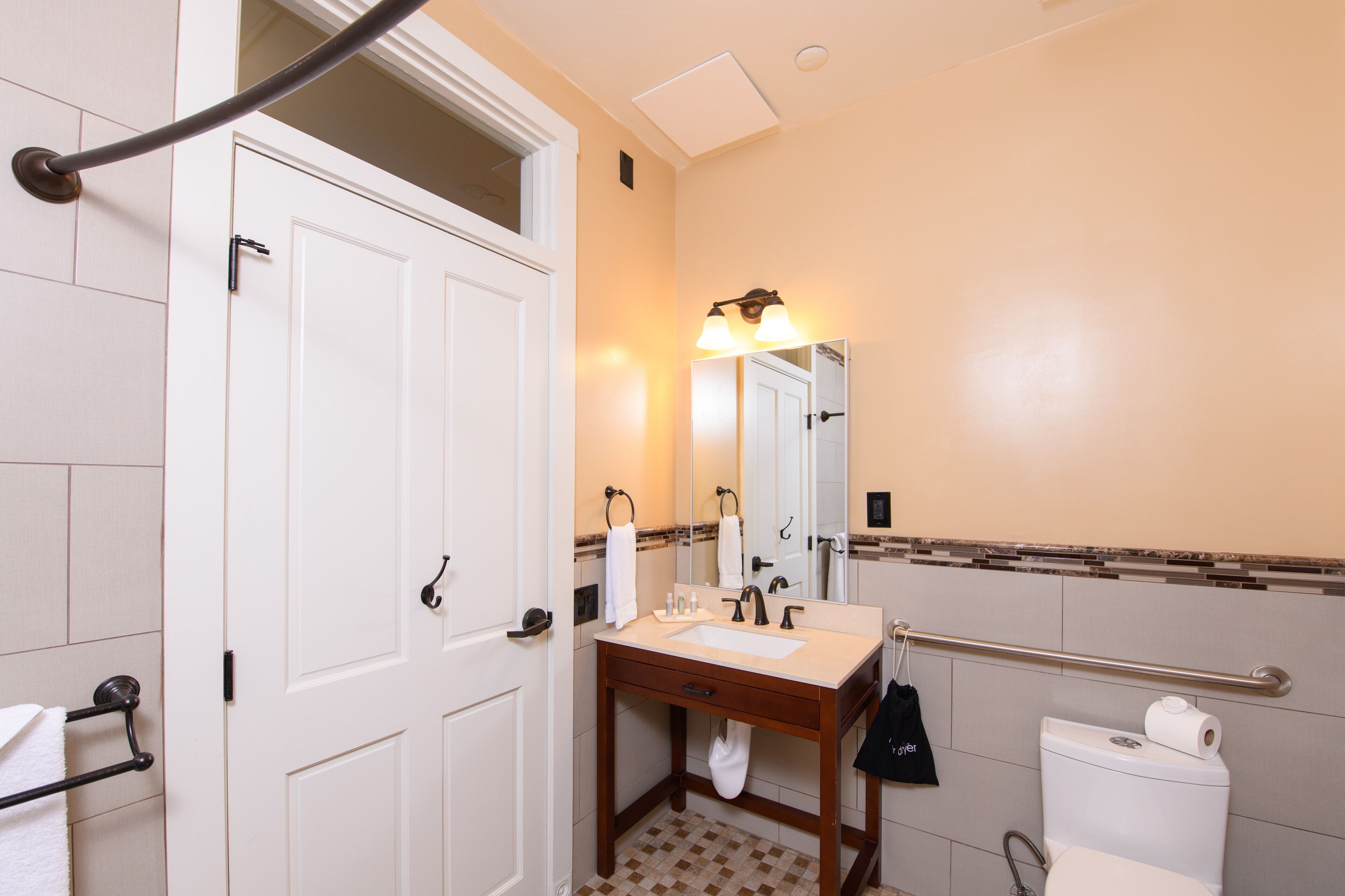 A bathroom with a white door, a sink with a mirror, a towel rack, and a toilet.