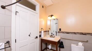 A bathroom with a white door, a sink with a mirror, a towel rack, and a toilet.