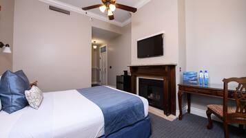 A hotel room with a bed, a desk, a television, and a fireplace.