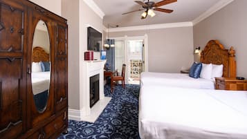 A hotel room with a large wooden wardrobe, a fireplace, two beds, a ceiling fan, and a balcony with a view.