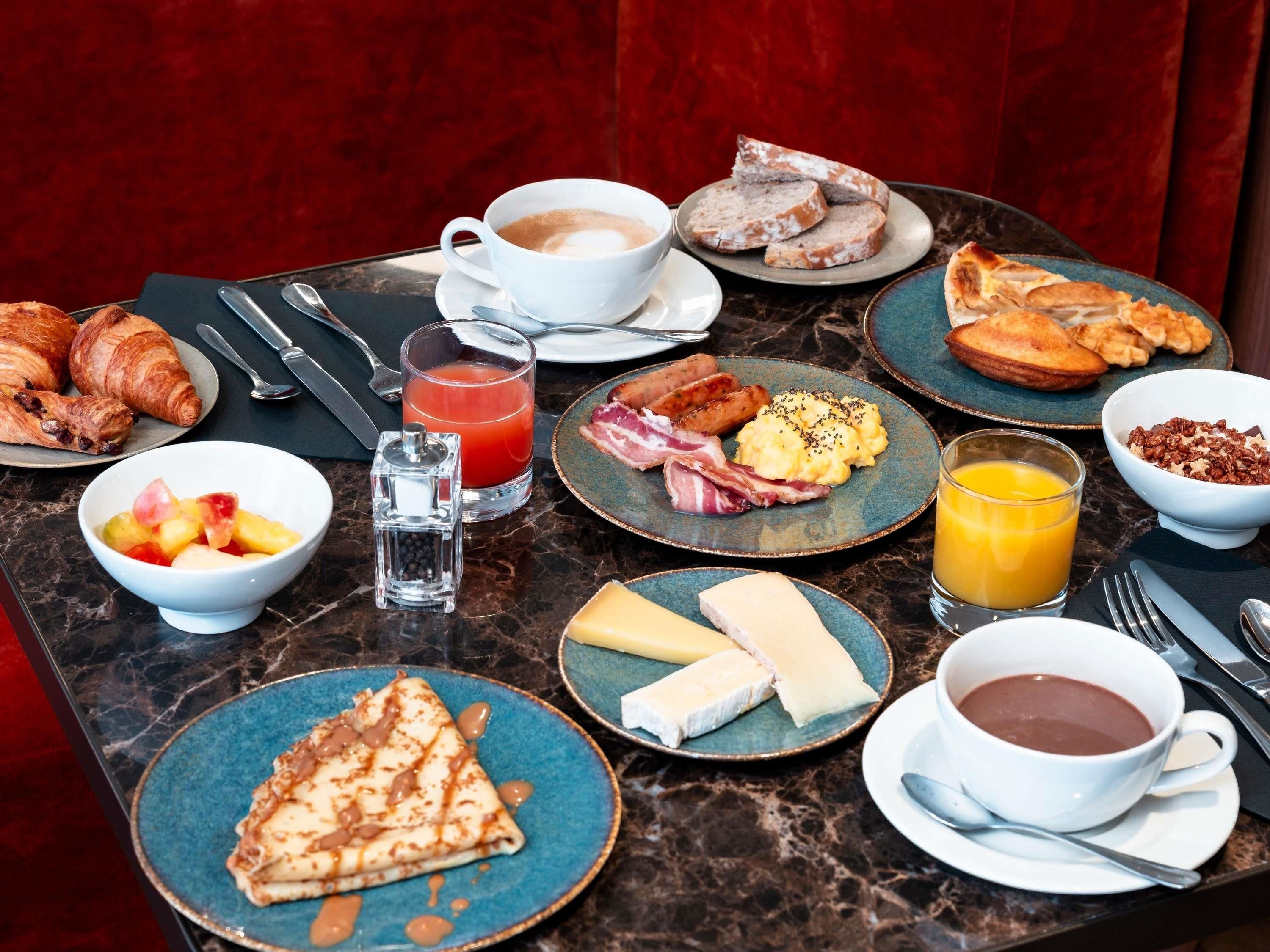 Una tavola imbandita per la colazione, con croissant, salsicce, uova e diverse bevande.