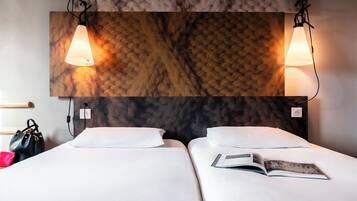 Une chambre d’hôtel avec deux lits, une tête de lit à motifs de marbre et deux lampes fixées au mur.