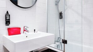 A modern bathroom with a white sink, a red towel, a black circular mirror, and a glass shower enclosure.