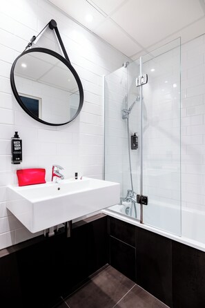 A modern bathroom with a white sink, a red towel, a black circular mirror, and a glass shower enclosure.