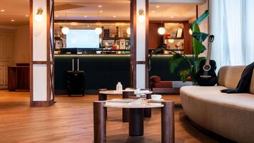 A modern hotel lobby with a reception desk, a seating area with a sofa and a coffee table, and a large plant.
